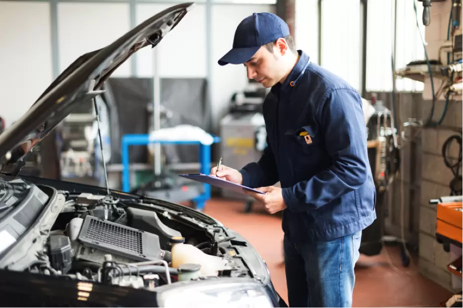 Technician inspecting a vehicle engine bay with clipboard
