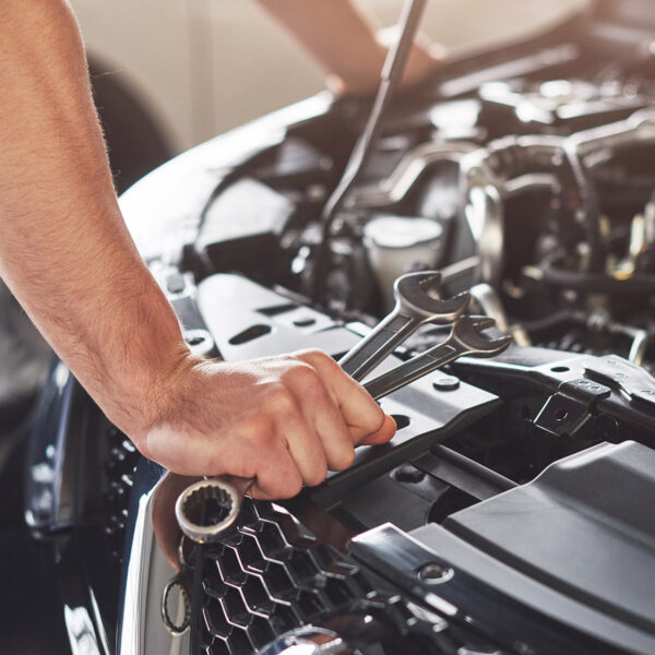 Mechanic holding wrenches over an open engine bay